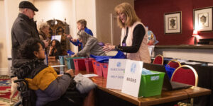 Conference registration desk with a person standing in the background, and a person in a wheelchair in the foreground with a woman handing them name badges.